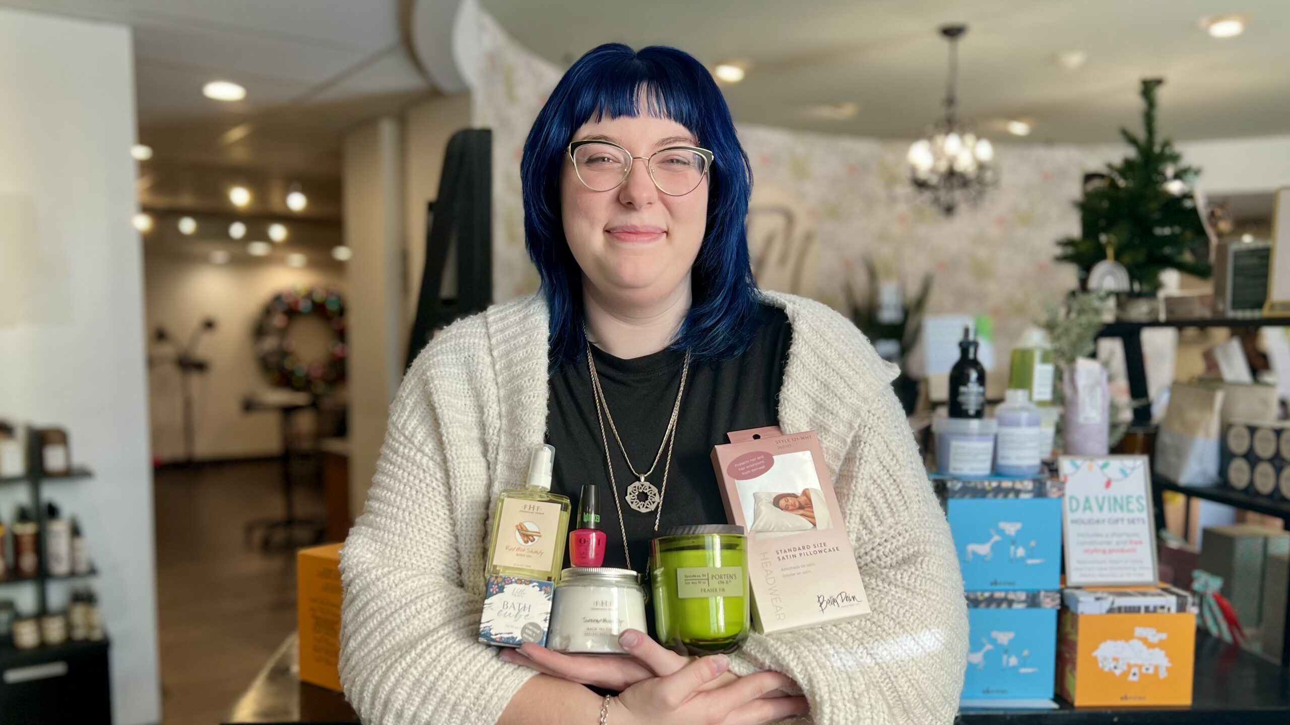 Our guest services manager Becca holds six self-care essentials from Tyler Mason to cozy up with this winter: Villa Bain Bath Cube, FarmHouse Fresh Red Hot Shandy Body Oil, Serene Moon Dip Body Mousse, OPI Wicked Collection nail polish, Porten's on 15th's Fraser Fir candle, and Headwear's white satin pillowcase.