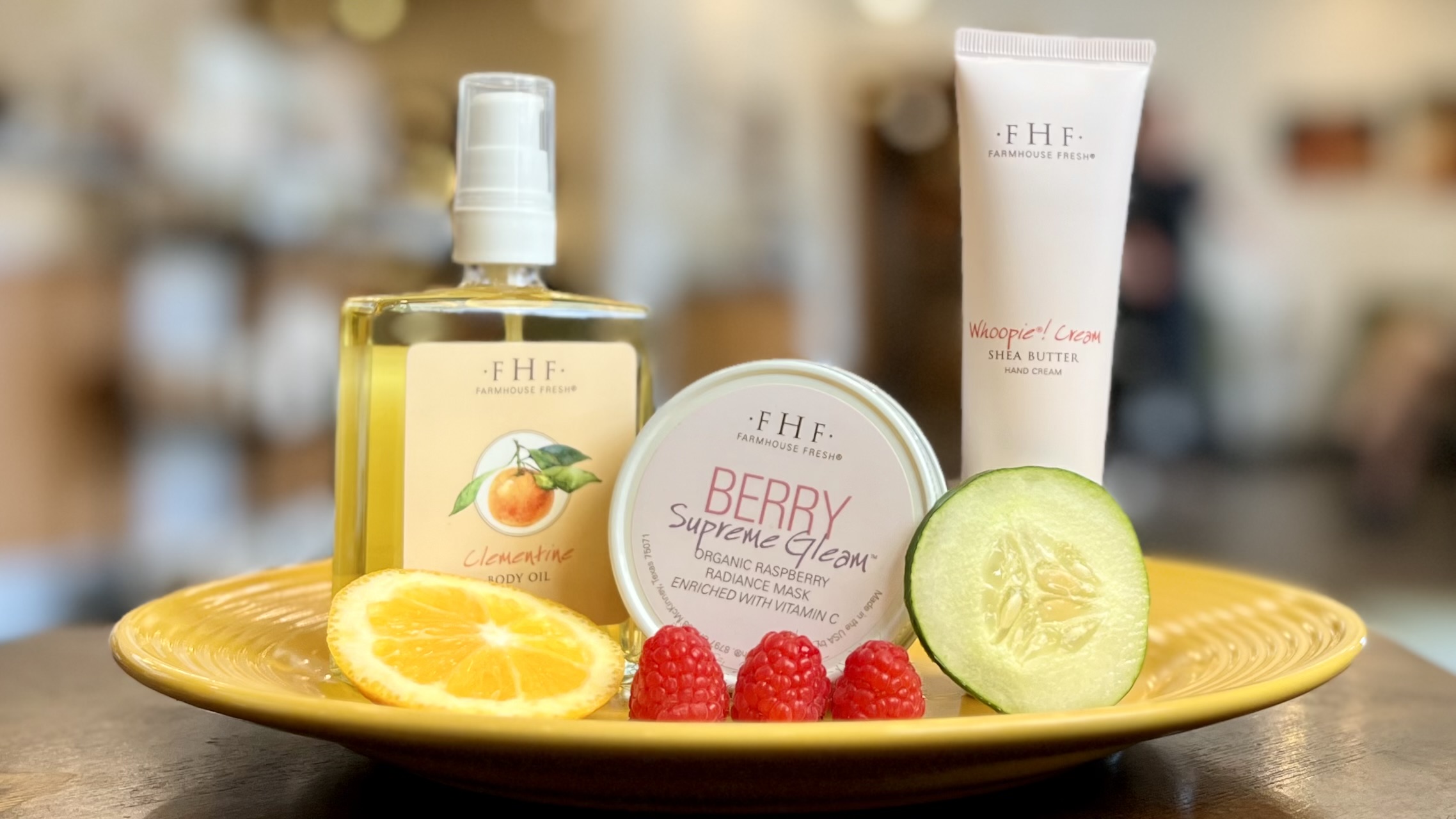 FarmHouse Fresh's Clementine Body Oil, Berry Supreme Gleam Radiance Mask, and Fluffy Bunny Shea Butter sit on a plate with an orange slice, cucumber slice, and raspberries.