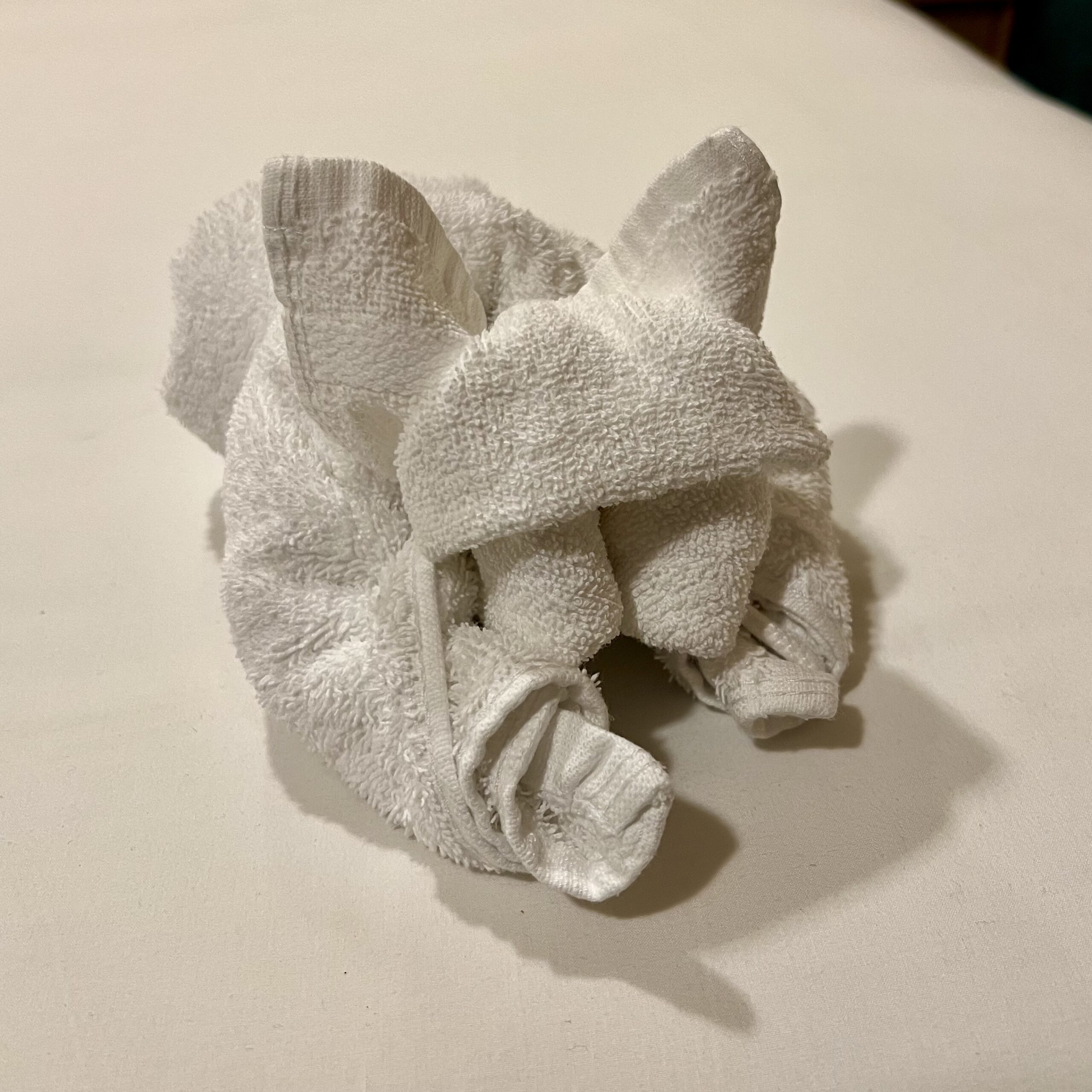 A dog-shaped towel sits on our bed's white sheets in our stateroom.