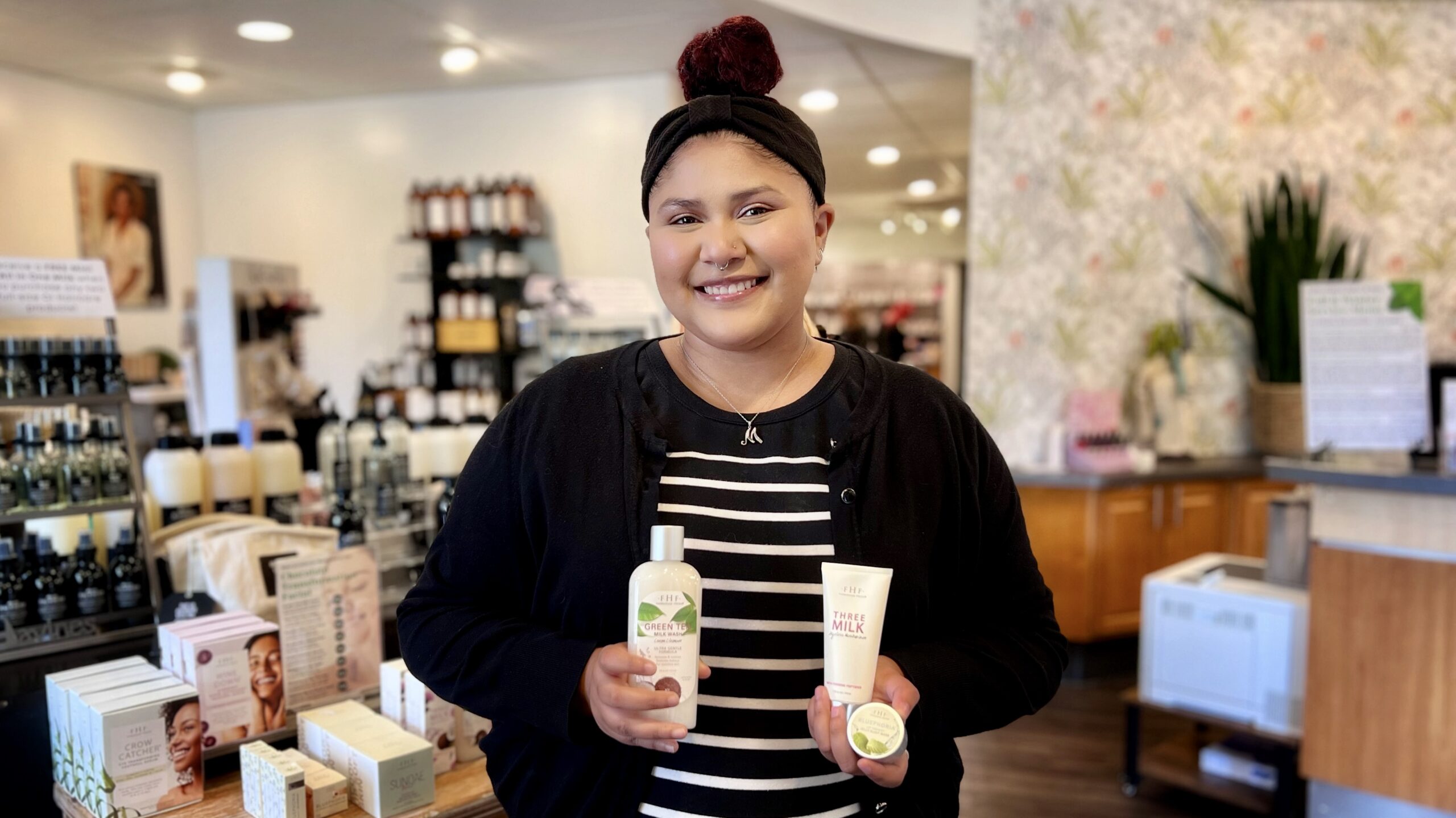 Our guest services representative Madison smiles as she holds FarmHouse Fresh's Green Tea Milk Wash Cream Cleanser, Three Milk Ageless Moisturizer, and Bluephoria Lip Drench Sleep Mask.