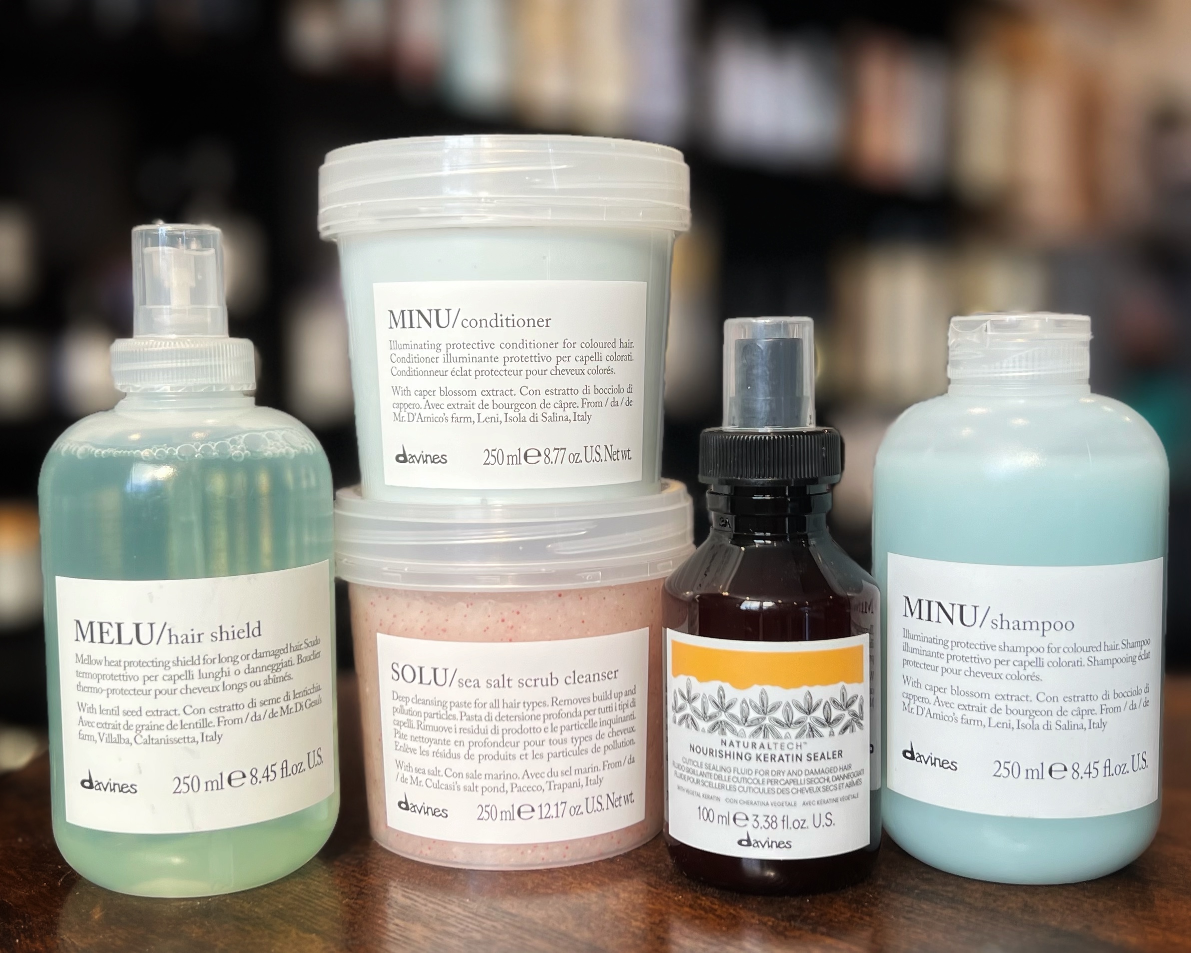 Our marketing manager Nicole's fall hair care routine is displayed on a brown table, including Davines' Melu Hair Shield, Solu Sea Salt Scrub, Minu Shampoo and Conditioner, and Naturaltech Nourishing Keratin Sealer. 