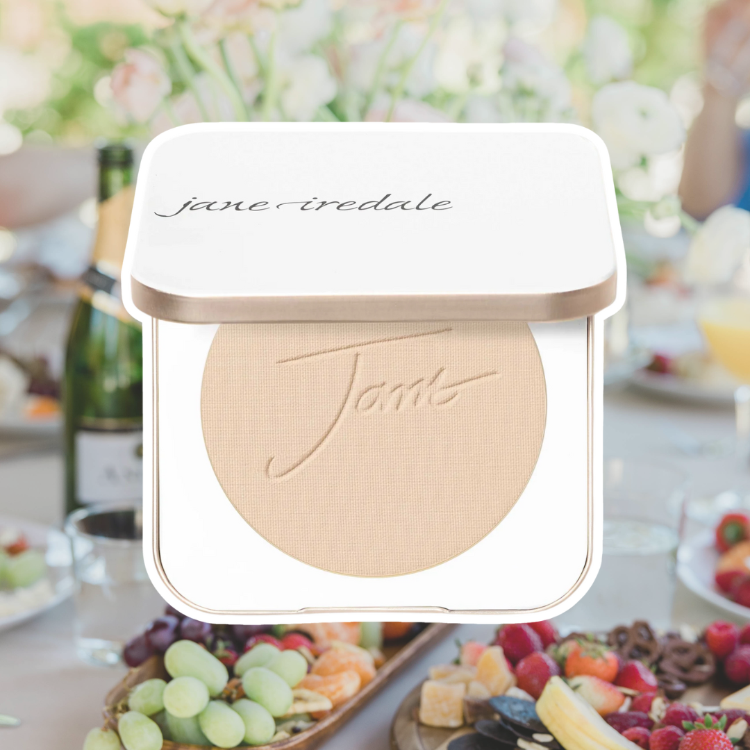 Jane Iredale's PurePressed Base Mineral Foundation against a background of a brunch spread with fruit, cheese, pretzels, and champagne.
