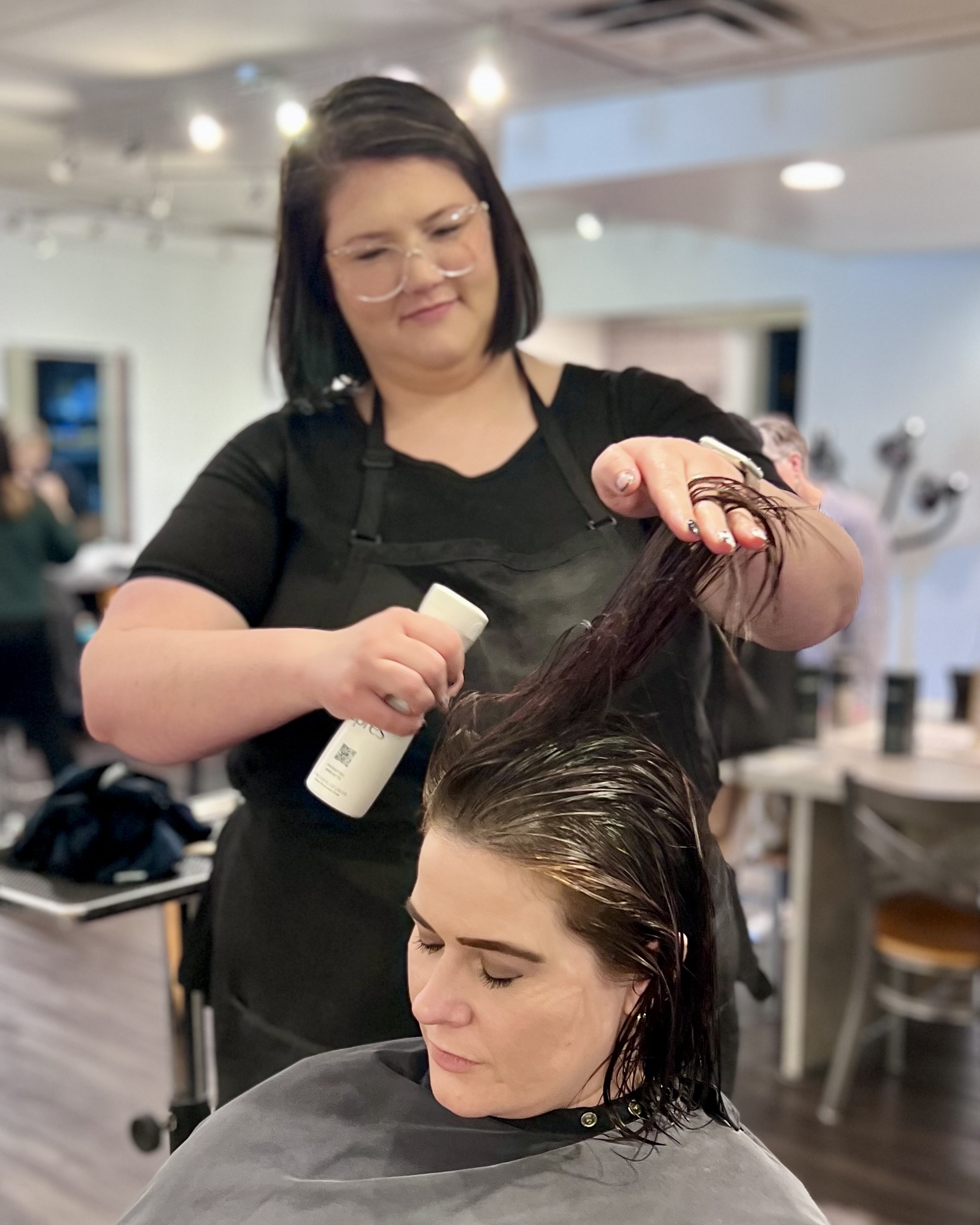 Our stylist Emily sprays Epres' Bond Repair Treatment onto our stylist Rachel's hair during her Bond Repair Treatment Blowout.