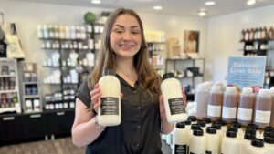 Our guest services representative Emma holds Davines' OI shampoo and conditioner liters that are 20% off while supplies last for our annual Liter Sale.