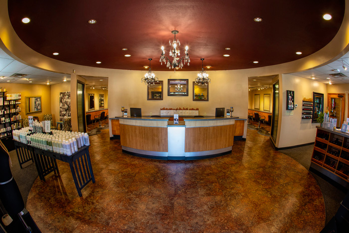 Spacious salon lobby with a curved reception desk, chandelier lighting, product displays, and framed art on beige walls. - Tyler Mason Salon + Spa in Indianapolis, IN