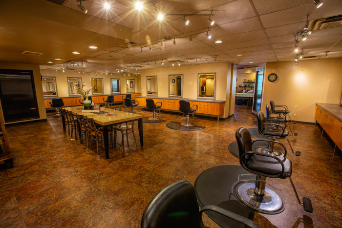 A spacious, well-lit hair salon with empty styling chairs, large mirrors, and a central wooden table under ceiling lights. - Tyler Mason Salon + Spa in Indianapolis, IN