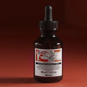 An Energizing Thickening Tonic (Copy) in a dark glass dropper bottle with a detailed label stands on a red surface against a matching red background. - Tyler Mason Salon + Spa in Indianapolis, IN